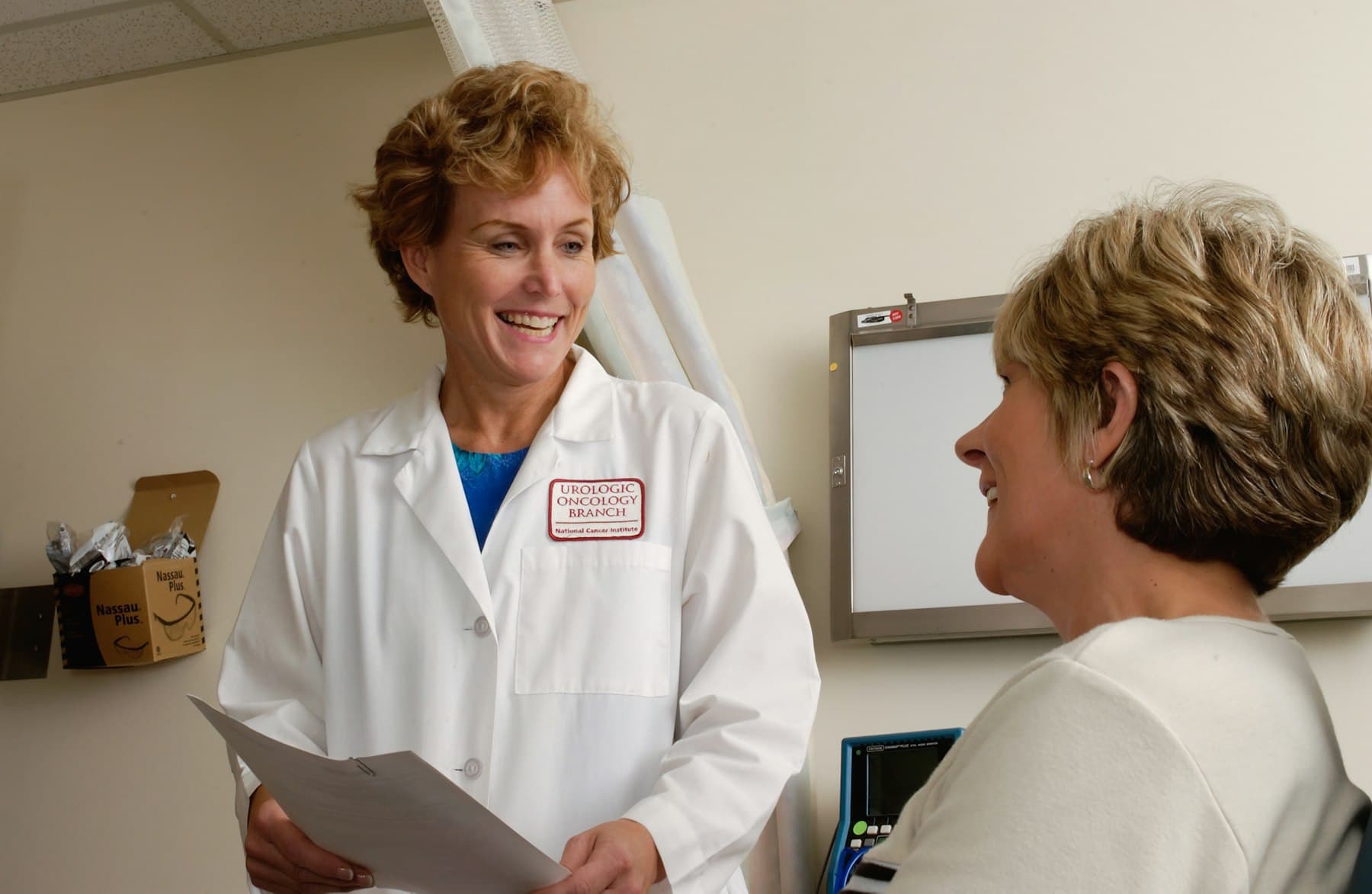 A smiling doctor talks with a patient in an exam room